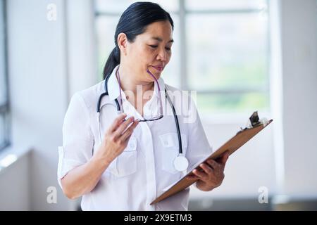 Medico donna asiatica che esamina le registrazioni dei pazienti in ambiente ospedaliero Foto Stock