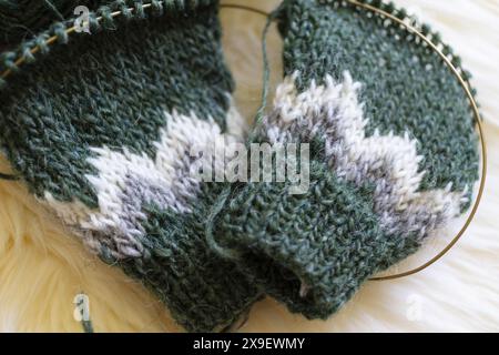 Foto ravvicinata delle maniche del maglione in maglia di lana islandese verde, grigio e bianco in corso con tecnica magica ad anello Foto Stock