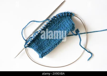Fotografia da tavolo di un progetto di maglieria blu turchese con punti stockinette su aghi circolari su sfondo bianco Foto Stock
