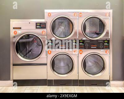 Asciugatrici industriali con pannelli di controllo digitali in lavanderia self-service, allineate e numerate. Foto Stock