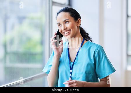 Medico sorridente che indossa scrub e parla al telefono in ospedale Foto Stock