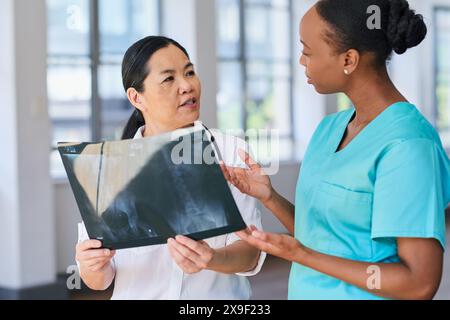 Team medico diversificato che discute i risultati dei raggi X in ambiente ospedaliero Foto Stock