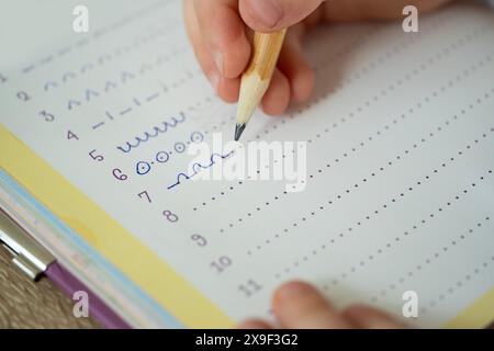 Primo piano con la mano del bambino, pratica la scrittura delle prime lettere su un notebook, istruzione e alfabetizzazione Foto Stock