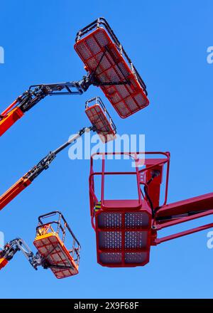 Gruppo numeroso di gru articolate, cestelli e bracci idraulici in alto in un cielo azzurro, con prospettiva ad angolo basso. Foto Stock