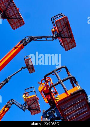 Gruppo numeroso di gru articolate, cestelli e bracci idraulici in alto in un cielo azzurro, con prospettiva ad angolo basso. Foto Stock