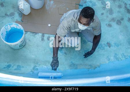 Lavoratore che utilizza un rullo per applicare la vernice in gel di vetroresina su una vecchia piscina. Foto Stock