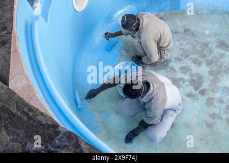 Operai che utilizzano rulli per applicare vernice con gel di fibra di vetro su una vecchia piscina. Foto Stock