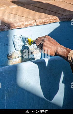 Lavoratore che utilizza un pennello per applicare la vernice con gel in fibra di vetro su una vecchia piscina. Foto Stock