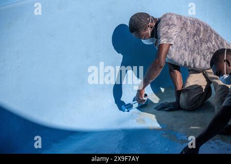 Operai che utilizzano rulli per applicare vernice con gel di fibra di vetro su una vecchia piscina. Foto Stock