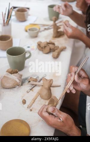 Mani ravvicinate di uno scultore maschio che forma una statuina di un gatto gattino di argilla Foto Stock