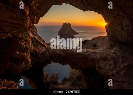 Vista dell'isolotto di es Vedra attraverso una grotta rocciosa al tramonto, Sant Josep de sa Talaia, Ibiza, Isole Baleari, Spagna Foto Stock