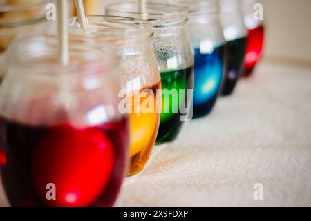 Primo piano di una fila di vasetti di vetro riempiti con colorante multicolore per mordere le uova di Pasqua Foto Stock