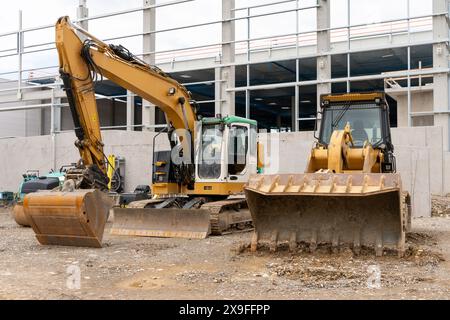 Escavatore e bulldozer in piedi presso il cantiere di fronte a una nuova costruzione in cemento. Foto Stock