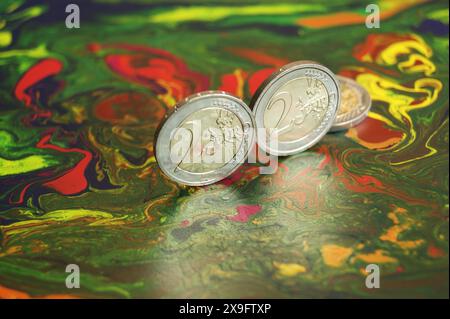 Nuove e brillanti monete da 2 euro su una superficie astratta a chiazze. Foto Stock