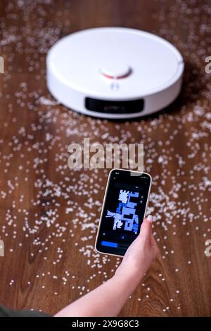 Giovane donna che usa lo smartphone per controllare l'aspirapolvere robot intelligente. Foto Stock