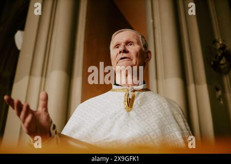 Vista dall'angolo basso del sacerdote caucasico anziano in piedi di fronte al leggio nella chiesa cattolica che parla ai visitatori Foto Stock