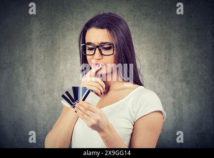 Giovane donna in dubbio che sceglie una carta di credito da usare Foto Stock