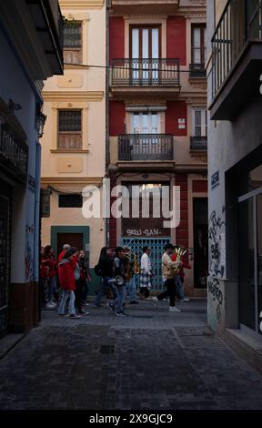 Il gruppo in giacche rosse cammina attraverso uno stretto vicolo fiancheggiato da graffiti a Valencia, in mezzo all'architettura storica, durante i festeggiamenti di las fallas. Foto Stock