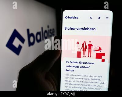 Persona che detiene un cellulare con pagina web della compagnia di assicurazioni svizzera Baloise Holding AG davanti al logo aziendale. Messa a fuoco al centro del display del telefono. Foto Stock