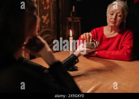 Vista posteriore dell'irriconoscibile misterioso indovinello che mischiava le carte dei tarocchi e chiedeva alla donna cliente di spostare il mazzo di carte per la disposizione durante la sessione Foto Stock