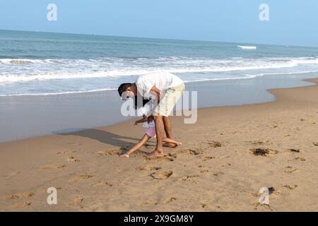 Tra dolci onde, un padre assiste sua figlia per iscritto sulla spiaggia sabbiosa. La loro amorevole interazione cattura l'essenza del tempo in famiglia da parte del Foto Stock