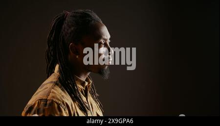 Persona afroamericana sorpresa di vedere qualcosa in studio, di essere stupita e di ammirare la vista su sfondo nero. Modello maschile che si guarda intorno e si sente scioccato, dicendo wow. Foto Stock