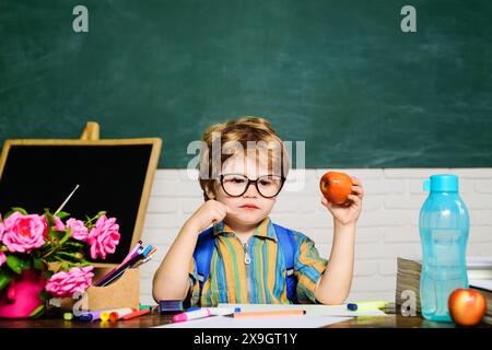 Pranzo a scuola durante la pausa. Piccolo studente che pranza con la mela in classe. Allievo della scuola elementare seduto a tavola a mangiare mela a. Foto Stock