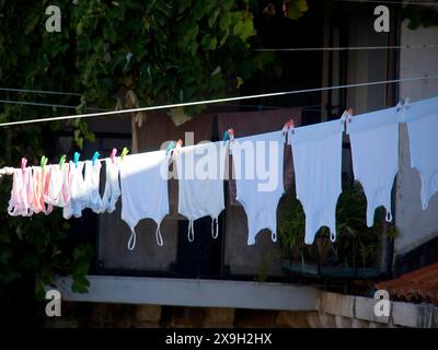 Asciugamani bianchi appesi su una linea di lavaggio, fissati da clip colorate, sullo sfondo un balcone con piante verdi, con la città vecchia di Dubrovnik Foto Stock