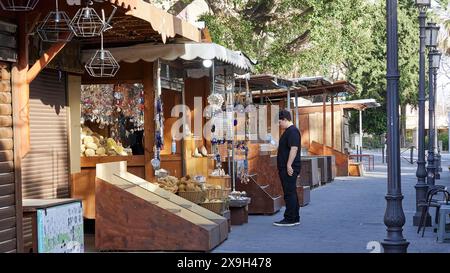 Negozi di souvenir, passerella per il Palazzo del Gran Maestro, Un vivace mercato con varie bancarelle lungo una strada con alberi, Young man, la città vecchia di Rodi Foto Stock