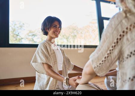Felice allenatore di yoga che tiene per mano una donna durante la sessione di guarigione olistica di gruppo. Foto Stock