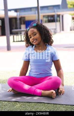 La ragazza birazziale pratica yoga all'aperto a scuola Foto Stock