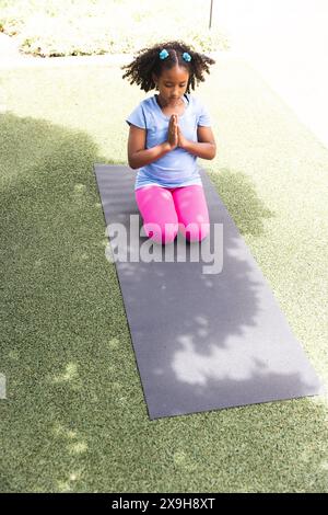 La ragazza birazziale pratica yoga all'aperto a scuola Foto Stock