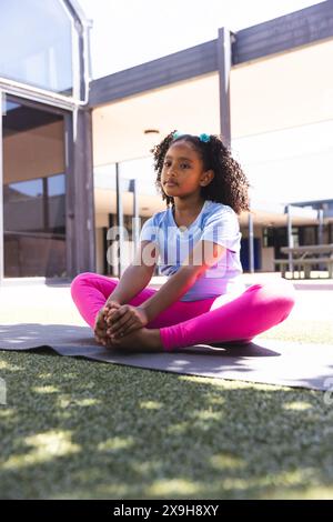 La ragazza birazziale pratica yoga all'aperto a scuola, con spazio per le copie Foto Stock