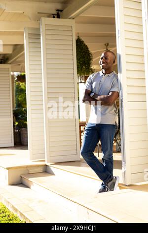 All'aperto, giovane afroamericano in piedi sul portico, sorridendo con le braccia incrociate Foto Stock