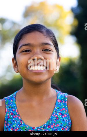 All'aperto, giovane ragazza birazziale che sorride brillantemente, indossa un colorato abito floreale Foto Stock