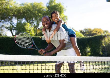 All'aperto, padre e figlia diversi sul campo da tennis con lussureggianti alberi verdi Foto Stock