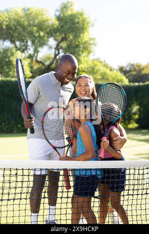 All'aperto, una famiglia di quattro persone sorride e tiene racchette da tennis nelle giornate di sole Foto Stock
