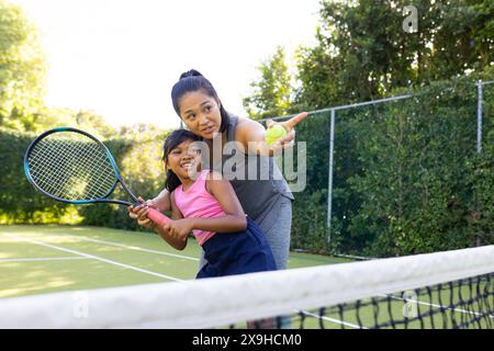 All'aperto, madre e figlia birazziali giocano a tennis insieme nelle giornate di sole Foto Stock