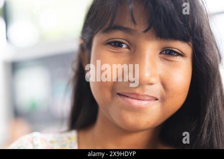 Ragazza birazziale con un sorriso gentile, i suoi capelli scuri cadono dolcemente intorno al viso in una classe scolastica Foto Stock