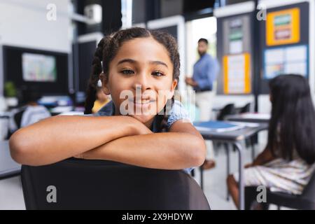 Ragazza birazziale con i capelli intrecciati sorride in una classe scolastica Foto Stock