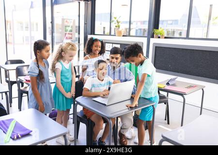 Un giovane insegnante asiatico maschile guida i bambini intorno al laptop Foto Stock