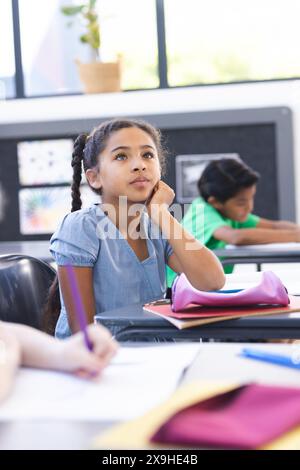 A scuola, una giovane studentessa birazziale sta pensando, un'altra studiando in classe Foto Stock