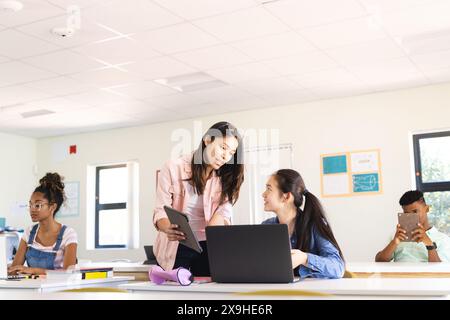 Una giovane insegnante birazziale insegna in una luminosa classe alle superiori Foto Stock