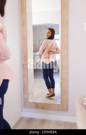 Una giovane donna birazziale che indossa jeans e top rosa, in piedi a casa Foto Stock