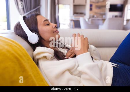 Una giovane donna birazziale che indossa le cuffie e si rilassa a casa Foto Stock