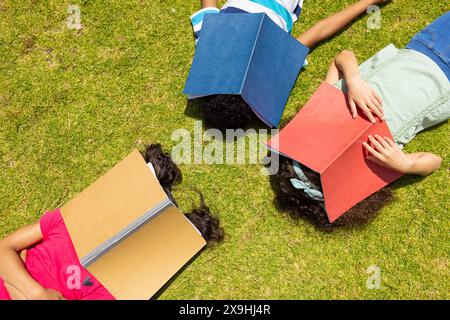 Tre bambini sono sdraiati sull'erba leggendo libri, con particolare attenzione all'istruzione e al tempo libero Foto Stock