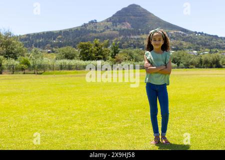 Una ragazza birazziale si trova in un parco soleggiato sullo sfondo di una montagna, con spazio fotocopie Foto Stock