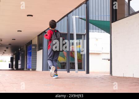 A scuola, ragazzo birazziale che cammina lungo il corridoio con spazio per le copie all'aperto Foto Stock