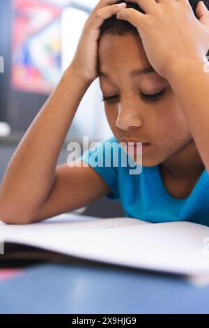 Un ragazzo birazziale studia intensamente in classe a scuola Foto Stock