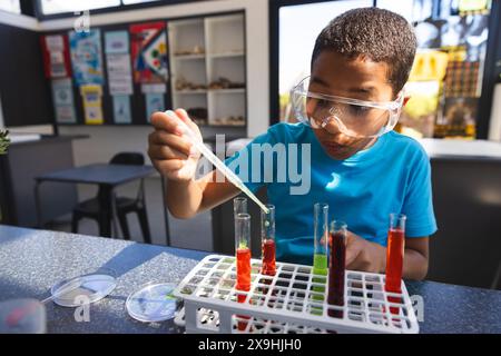 Un ragazzo birazziale si impegna in un esperimento scientifico a scuola in classe Foto Stock